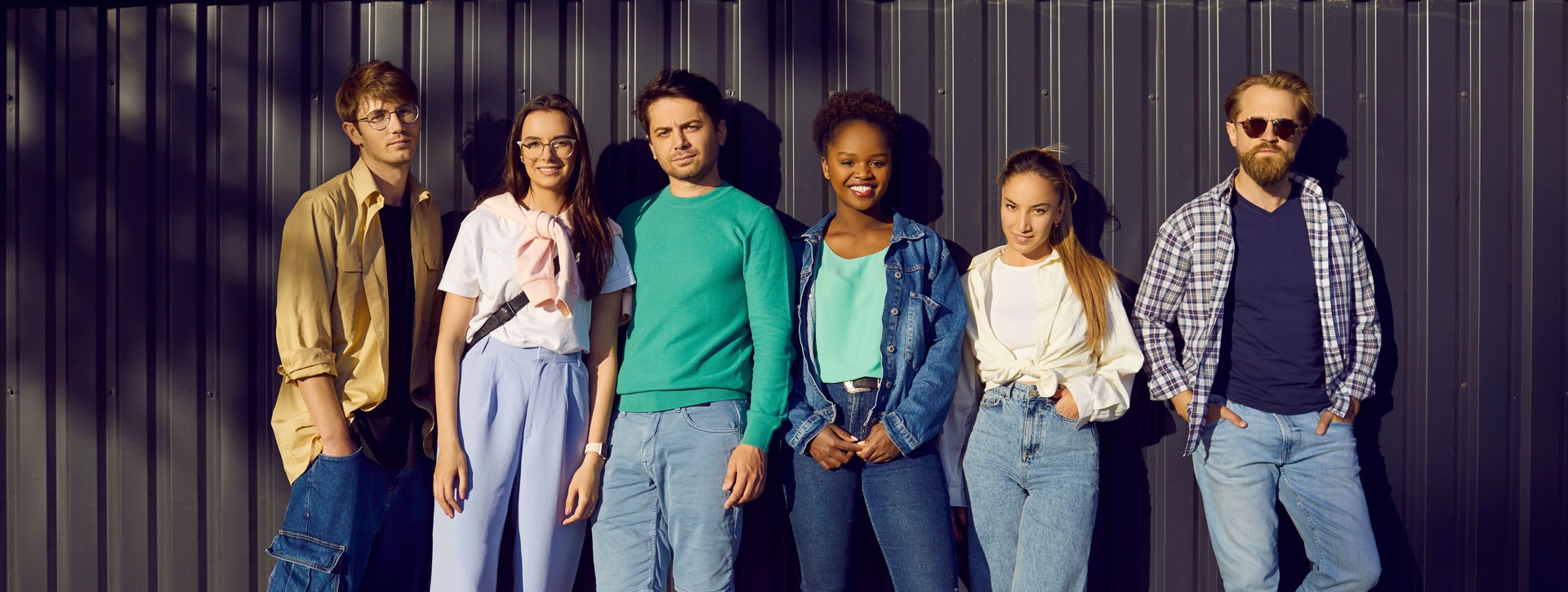 Diverse group of young people wearing comfortable casual clothes standing by street wall